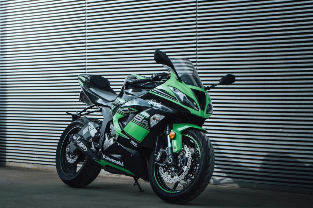 A vibrant green Kawasaki Ninja motorcycle parked outdoors against a modern corrugated metal wall.