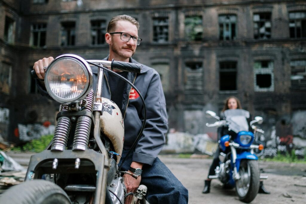 Two bikers pose with motorcycles outside an abandoned building, exuding a gritty urban vibe.